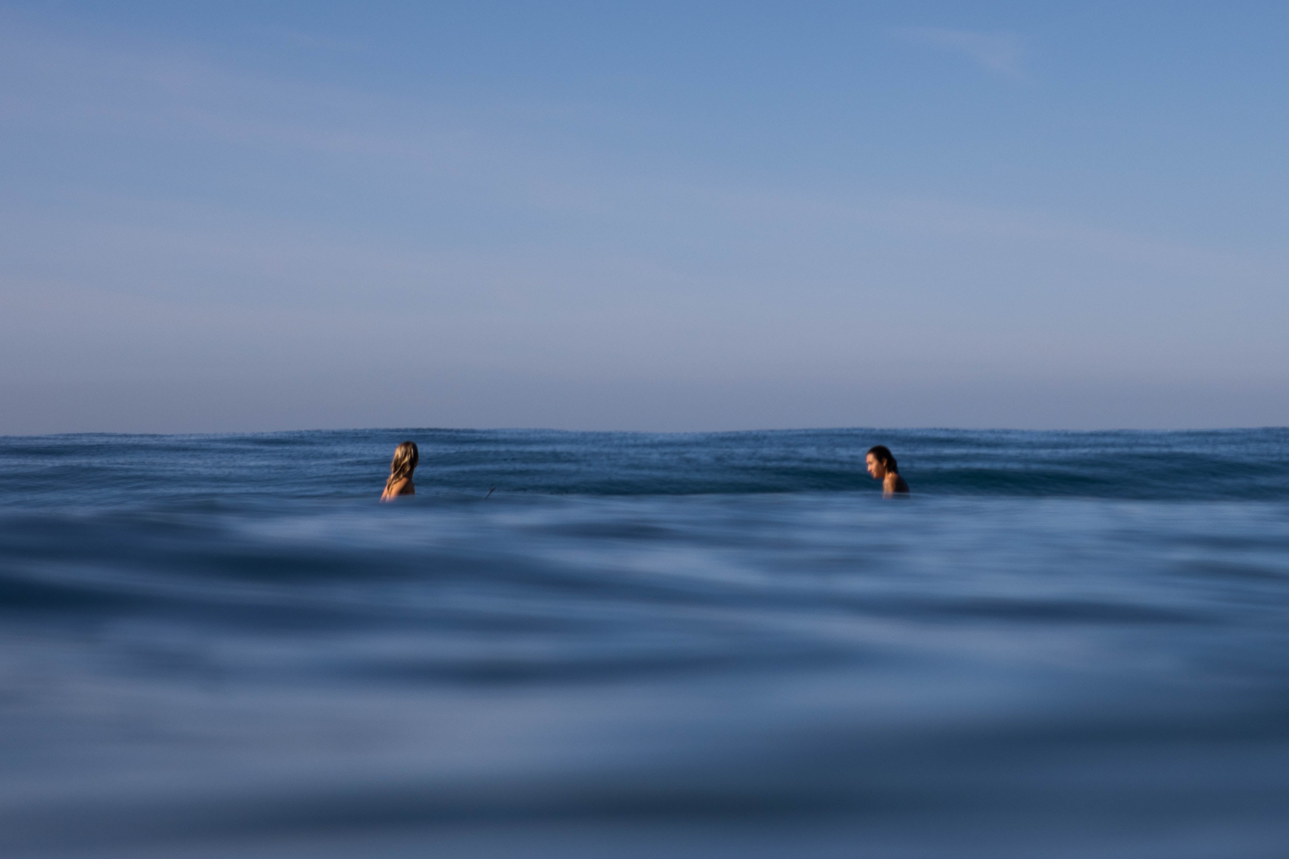 two female surfers sitting in the ocean facing one another