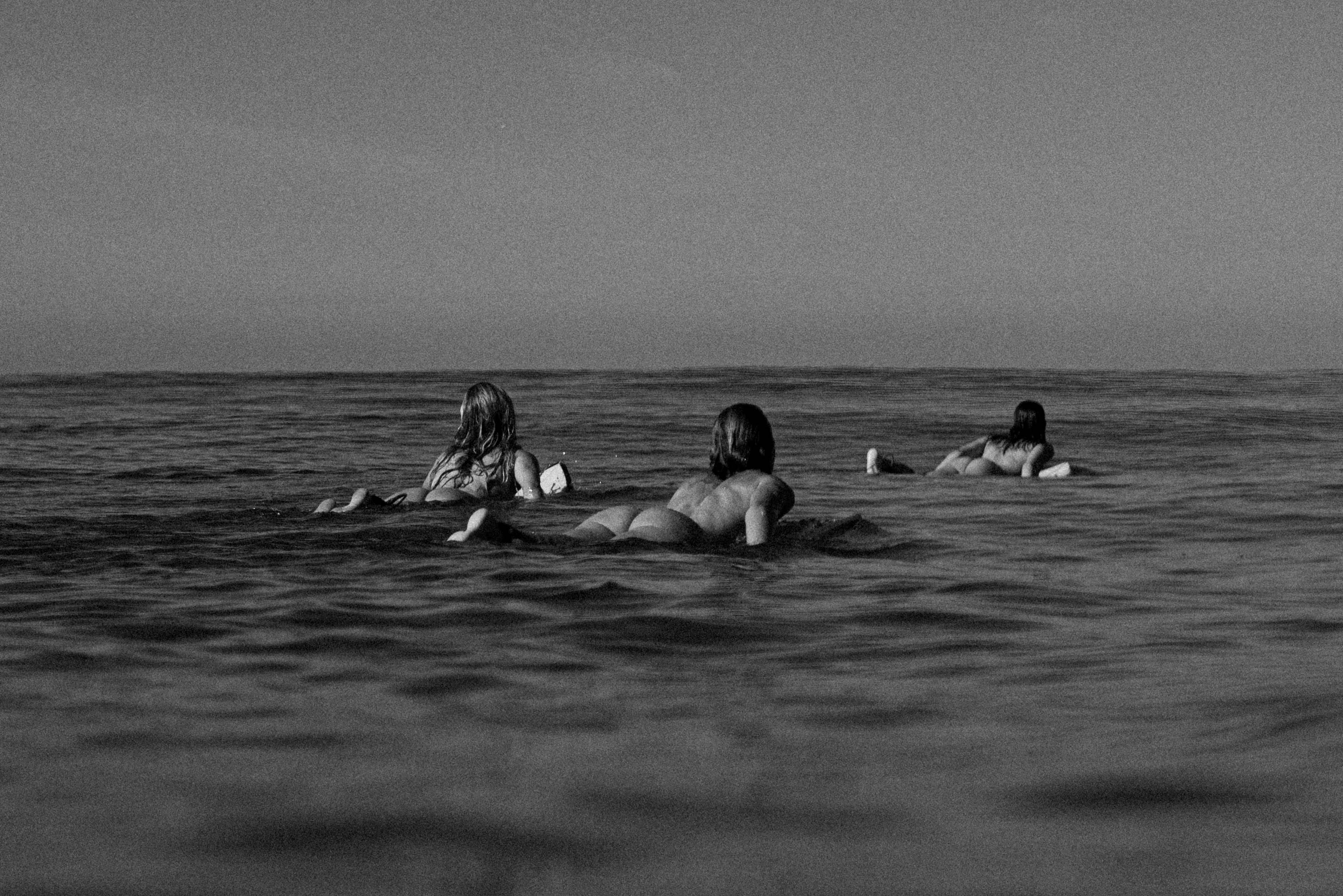 black and white photo of three nude female surfers paddling out to surf